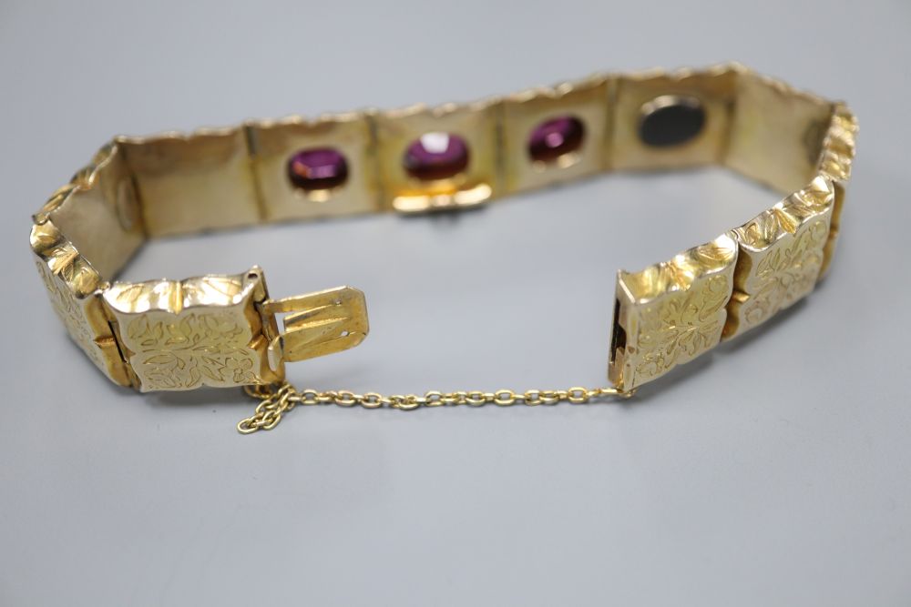 A Victorian engraved yellow metal and three stone garnet set hinged panel bracelet, with safety chain, gross 21.7 grams.